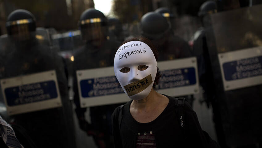 Una mujer con una máscara se encuentra frente a la policía antidisturbios que acordona la zona durante una protesta contra la Ley de Seguridad Ciudadana